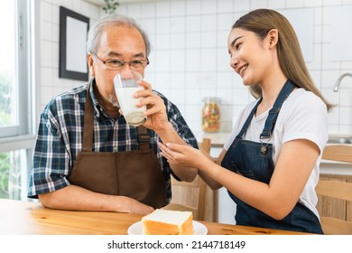 Asian Lovely Family, Young Daughter Prepare Breakfast For Older Father. Attractive Female Wear Apron Bake Bread Serve With Milk To Senior Elderly Dad Sitting On Eating Table In Kitchen At House.