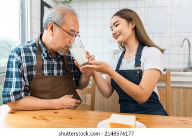 Asian Lovely Family, Young Daughter Prepare Breakfast For Older Father. Attractive Female Wear Apron Bake Bread Serve With Milk To Senior Elderly Dad Sitting On Eating Table In Kitchen At House.