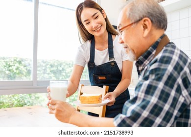 Asian Lovely Family, Young Daughter Prepare Breakfast For Older Father. Attractive Female Wear Apron Bake Bread Serve With Milk To Senior Elderly Dad Sitting On Eating Table In Kitchen At House.