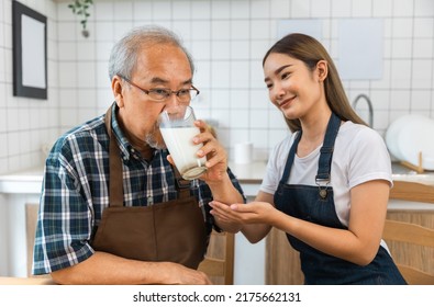 Asian Lovely Family, Young Daughter Prepare Breakfast For Older Father. Attractive Female Wear Apron Bake Bread Serve With Milk To Senior Elderly Dad Sitting On Eating Table In Kitchen At House.