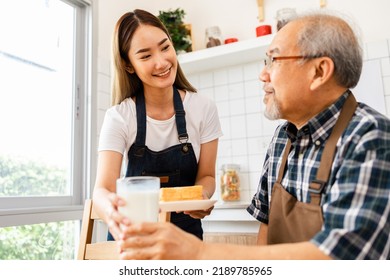 Asian Lovely Family, Young Daughter Prepare Breakfast For Older Father. Attractive Female Wear Apron Bake Bread Serve With Milk To Senior Elderly Dad Sitting On Eating Table In Kitchen At House.