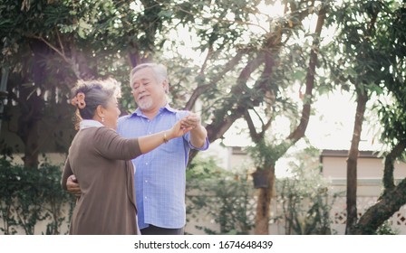 Asian Lovely Happy Senior Couple Grandfather And Grandmother Dancing Or Hugging Outside Of Home. Joyful Elderly Smiling Retired Lover Embracing Or Holding In Romantic Moment Of Love.