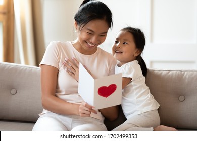 Asian lovely sweet preschool daughter congratulates mommy and life event birthday holiday  prepares for her handmade post card and red painted heart symbol unconditional love  Mother Day concept