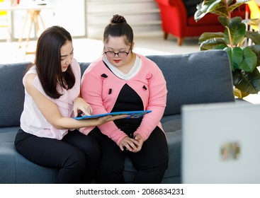 Asian lovely young mother smiling taking care and using alphabet puzzle toy teaching a girl with down syndrome daughter wearing eyeglasses on sofa in living room at home.