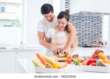 Asian Lovers Or Couple Cooking And Slicing Vegetable In Kitchen Room. Man And Woman Looking Each Other In Home. Holiday And Honeymoon Concept. Valentine Day And Wedding Theme