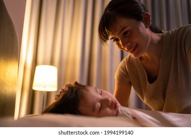 Asian Loving Beautiful Mother Look At Sleeping Young Small Comfortable Cute Kid With Gentle Eye. Caring Parent Mom Put Blanket On Sleeping Little Girl Daughter On Bed In Dark Bedroom At Night At Home.