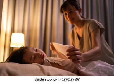 Asian Loving Beautiful Mother Take Care Asleep Young Small Comfortable Kid. Caring Parent Mom Put Blanket On Sleeping Little Girl Daughter On Bed In Dark Bedroom At Night. Parenting Activity At Home.