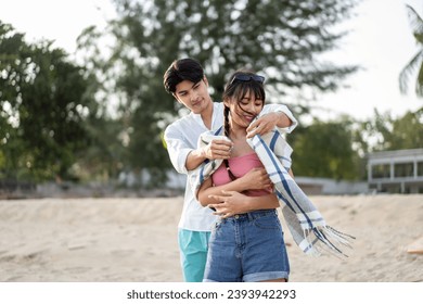 Asian loving boyfriend wrapped blanket on his girlfriend at the beach. Attractive young couple feel happy and enjoy spending leisure time at seaside enjoy holiday honeymoon trip in tropical sea island - Powered by Shutterstock