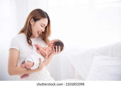 Asian Loving Mom Carying Of Her Newborn Baby At Home. Happy Mum Holding Sleeping Infant Child On Hands. Mother Hugging Her Little One Months Old Son.