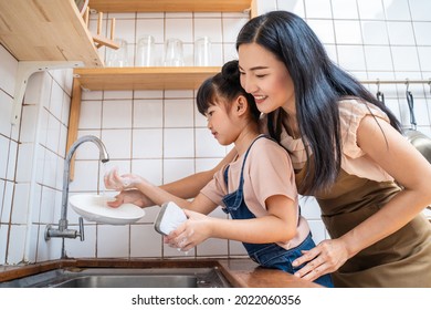 Asian loving mom teach young preschool girl to wash dishes in house. Happy family stay home in kitchen, Supportive mother spend time with little kid daughter together. Parenting Relationship concept.