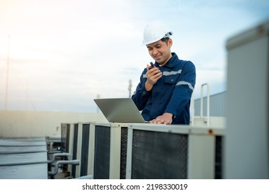 Asian Maintenance Engineer Wear Helmet Works On The Roof Of Factory. Supervisor Inspect Compressor System And Plans Installation Of Air Condition Systems In Construction Site Of Modern Buildings.