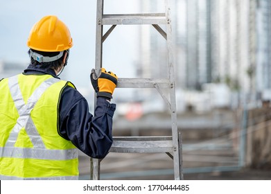 Asian Maintenance Worker Man With Safety Helmet And Green Vest Carrying Aluminium Step Ladder At Construction Site. Civil Engineering, Architecture Builder And Building Service Concepts