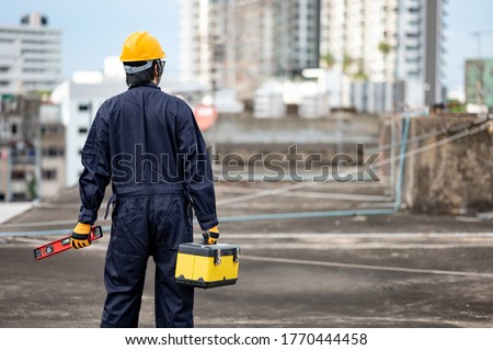 Asian maintenance worker man wearing protective suit and helmet holding red aluminium spirit level tool or bubble levels and work tool box at construction site. Equipment for civil engineering project