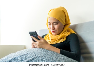 Asian Malay Girl Wearing Hijab Sitting In The Sofa Alone Using Smart Phone