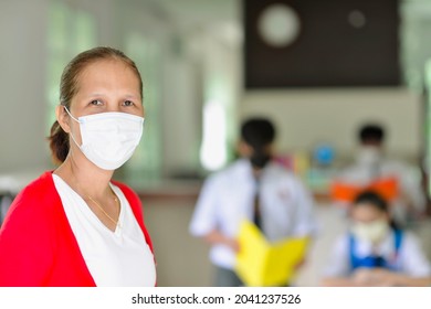 Asian Malaysian Teacher Wearing Mask During The Pandemic.Secondary Students Studying In Background While Wearing School Uniform And Face Mask.Tutor In Tuition Centre In Malaysia.