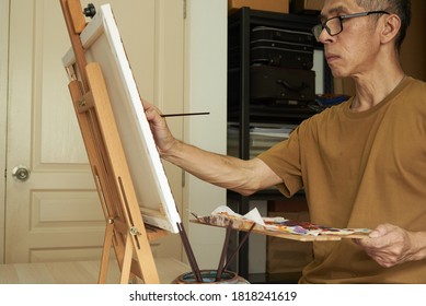 An Asian Male Adult Painting On The Canvas At Home