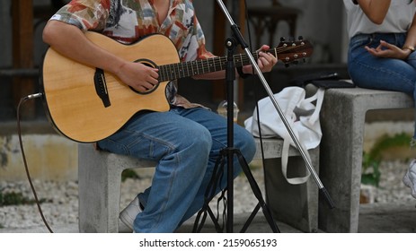 Asian male artist dressed like a hipster playing the guitar next to a microphone standing in the park. Music and abstract concepts. - Shutterstock ID 2159065193