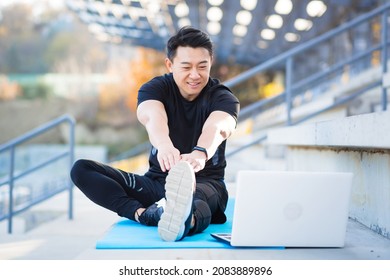 Asian Male Athlete Studies Online On The Help Of A Laptop Computer, Outside The Stadium In The Park, Performs Exercises On A Remote Fitness Course