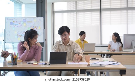 Asian Male Business Leader Explaining New Project And Discussing Corporate Business Plan With Colleague.