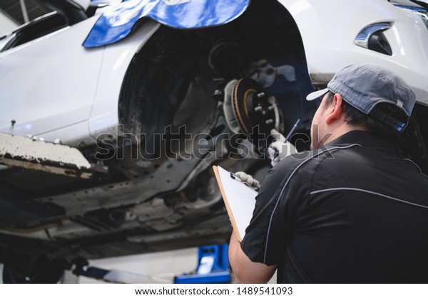 Asian male car technician car maintenance for
customers according to specified vehicle maintenance checklist.
Disk brake pad wear automotive repairing on vehicle. Safety
inspection check service