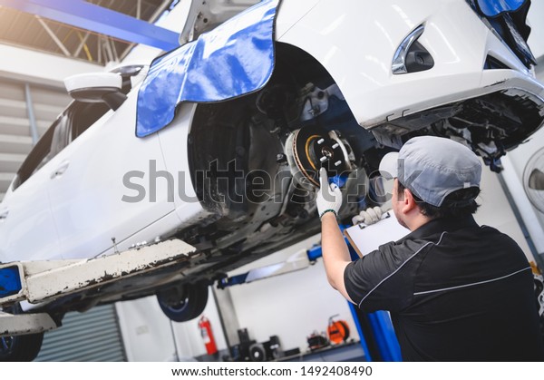 Asian male car technician car maintenance for\
customers according to specified vehicle maintenance checklist.\
Disk brake pad wear automotive repairing on vehicle. Safety\
inspection check service