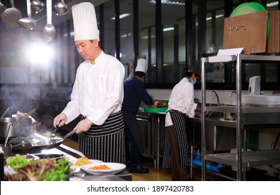 Asian Male Chef Cooking Food With His Colleuge In The Hotel Kitchen