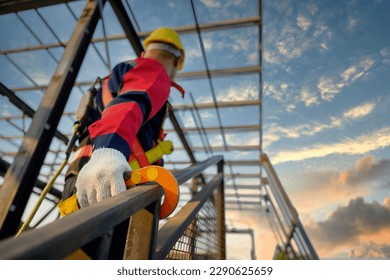 Asian male construction worker working at height on steel frame Wear safety gear and safety harness to work at high heights at the construction site.