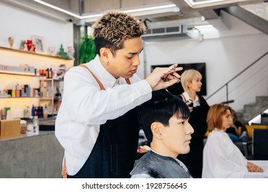 Asian male customer getting hair cut with hairdresser in salon. Fashionable barber using a scissor to trim client hair in barbershop - Powered by Shutterstock