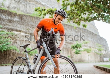 asian male cyclist checking his road bike tire