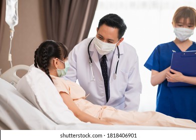Asiatischer männlicher Arzt tröstet und redet mit einer wiedergutmachenden Patientin während des Arztbesuchs im Krankenhaus mit weiblicher Krankenschwester im Hintergrund. Ärzte, die einen Mädchen besuchen.