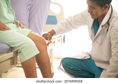 An Asian Male Doctor Examining The Reactions Of An Asian Male Patient. Neurologist Using A Knee Hammer Which Is A Medical Device For Physical Examination.