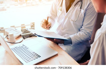 Asian Male Doctor Hand Holding Pen Writing Patient History List On Note Pad And Laptop For Looking Data Information.