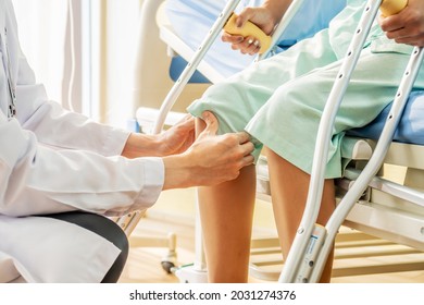 Asian Male Doctor Or Physiotherapist Examining Knee, Female Patient With Injured Leg Or Knee After Accident And Explain To Her The Diagnosis Of Problem In Clinic, Sport Exercise Injuries.