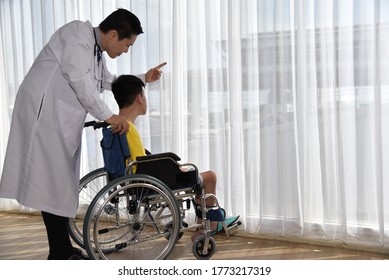 An Asian Male Doctor Taking Care And Look After Disabled Boy Patient /cripple Who Can Not Help Himself Sitting On Wheelchair In Hospital/Disability