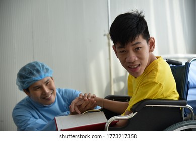 An Asian Male Doctor Taking Care And Look After Disabled Boy Patient /cripple Who Can Not Help Himself Sitting On Wheelchair In Hospital/Disability