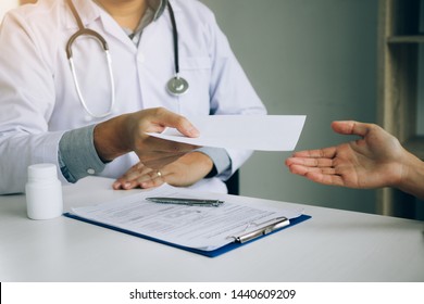 Asian Male Doctor Talking In Clinic Room And Handing A Prescription To The Patient.