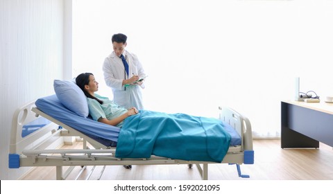 Asian Male Doctor Is Talking To Female Patients Lie In Bed In The Hospital Room About The Diagnosis Of Her Illness.disease Treatment And Health Care Concept