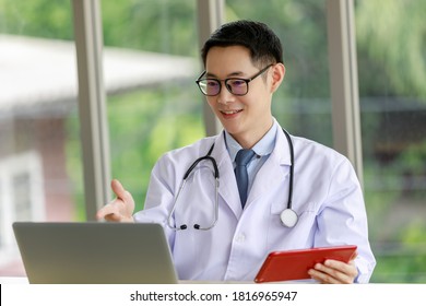 Asian Male Doctor Talking And Looking To Camera In Video Conference ,Positive Doctor Waving And Having Online Consultation On Digital Tablet Laptop