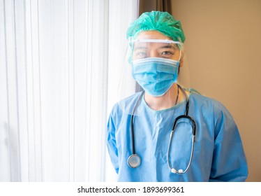 Asian Male Doctor Wearing Medical Gown With Face Shield And Mask Before Working In Operating Room In Hospital.