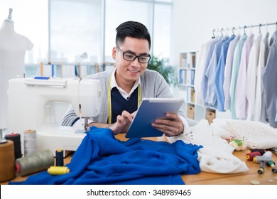 Asian male dressmaker reading something on tablet computer - Shutterstock ID 348989465