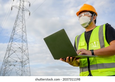 Asian Male Electrical Engineer Standing Holding Laptop Computer At Power Plant Young Electrical Engineer Working And Planning High Voltage Pole Inspection At The Electric Power Station