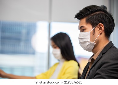 Asian Male Employee And Woman Co Worker Wearing Face Mask To Protect Virus Infection Typing On Laptop Computer At Office Desk. New Normal Working And Social Distancing Concept. Copy Space