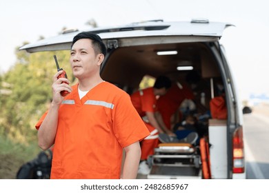 Asian male EMS paramedics or emergency medical technicians in orange uniforms holding portable radio while talking with emergency team sitting in ambulance - Powered by Shutterstock