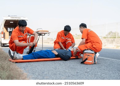 Asian male EMS paramedics or emergency medical technicians in orange uniforms performing first aid to patient on stretcher injured from road accident - Powered by Shutterstock