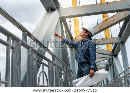 Asian male engineer standing on the bridge and is examining the strength of the bridge's structure, to people and engineering concept.