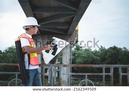 Asian male engineer standing on the bridge and looking at blueprint for planning to improve the structure, to people and engineering concept.