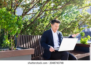 Asian Male Entrepreneur Freelancer Sitting Outdoors In City Park A Bench Talking Online A Video Call Using Laptop Business Man Office Worker Working On Urban Street Background Businessman Communicates