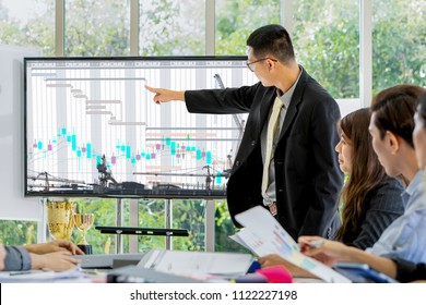 Asian Male Executive Having Meeting With Business Team To Plan And Follow Up Project Schedule By Presenting Project Grant Chart On Video Screen