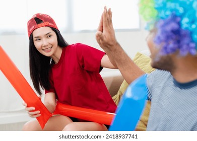 Asian male and female friends Watch the World Cup live broadcast on TV. Sports fans shout and hi five together, celebrating the sports team's victory. and eat snacks together at home - Powered by Shutterstock