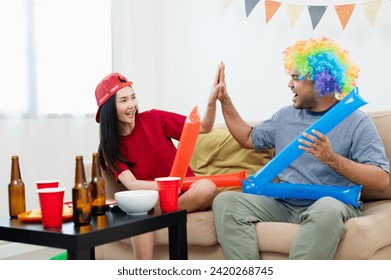 Asian male and female friends Watch the World Cup live broadcast on TV. Sports fans shout and hi five together, celebrating the sports team's victory. and eat snacks together at home - Powered by Shutterstock